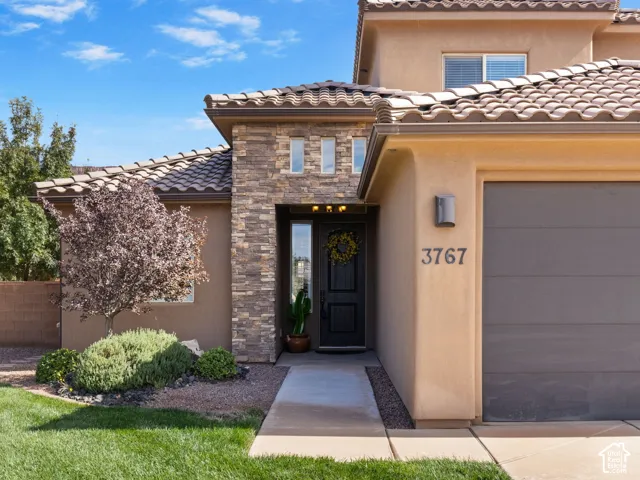 Stucco exterior featuring a prominent stone facade, tile roofing, and an integrated garage
