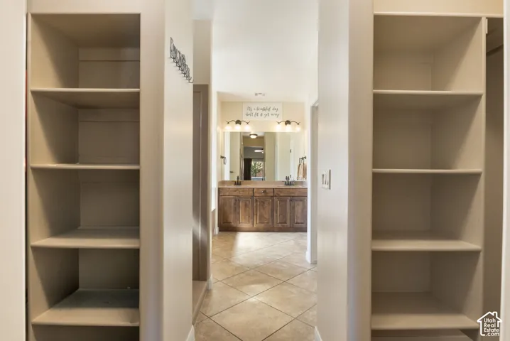Built-in shelving units, dual vanity with wood-finish cabinetry, countertop, and a tile floor