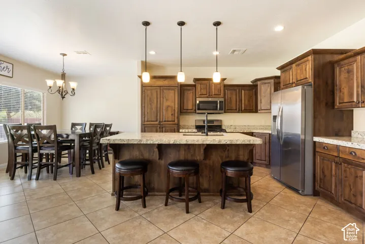 Spacious open-concept kitchen and dining area featuring rich wood cabinetry, stainless steel appliances, a large center island with seating for three, tile flooring, and pendant lighting
