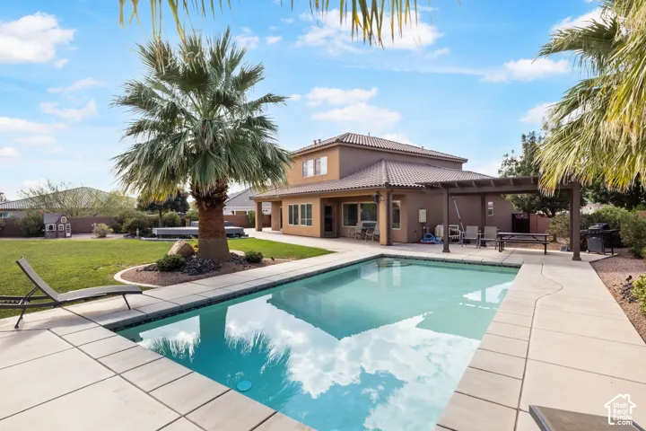 Expansive backyard featuring a rectangular swimming pool with concrete decking, a large pergola, and mature palm trees