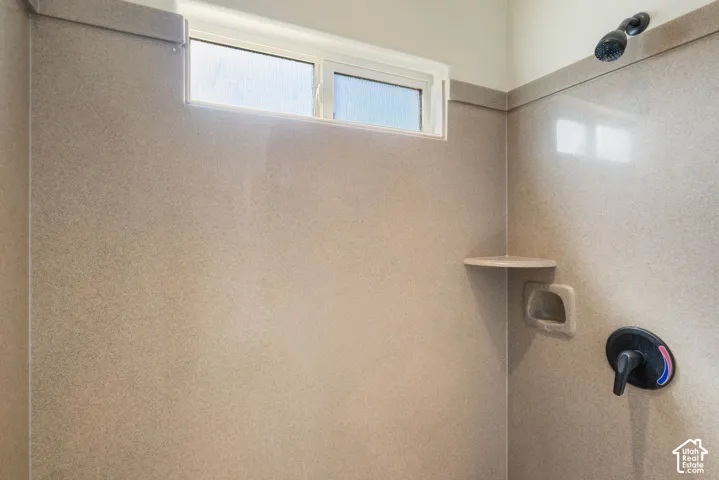 Shower enclosure with textured wall panels, corner shelving, built-in soap dish, and a transom window