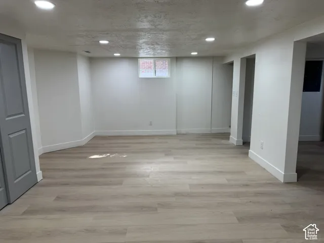 Recessed lighting illuminates the expansive room featuring wood-finish flooring, white walls, and a window with a brick exterior