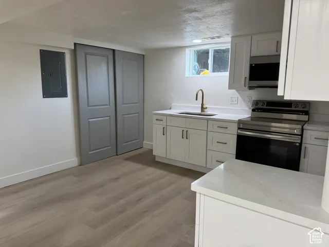White cabinetry with brushed nickel hardware, stainless steel appliances, solid surface countertops, light wood-finish flooring, and a brass-finish gooseneck faucet