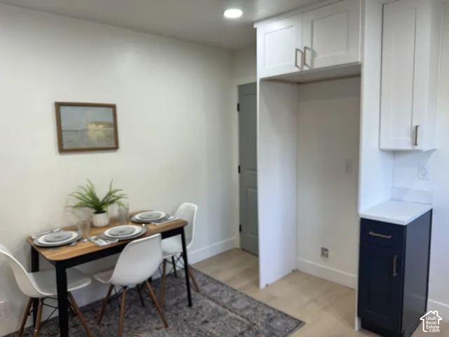 White shaker-style upper cabinetry with modern hardware, contrasting dark lower cabinetry, light-toned wood-finish flooring, and a solid surface countertop