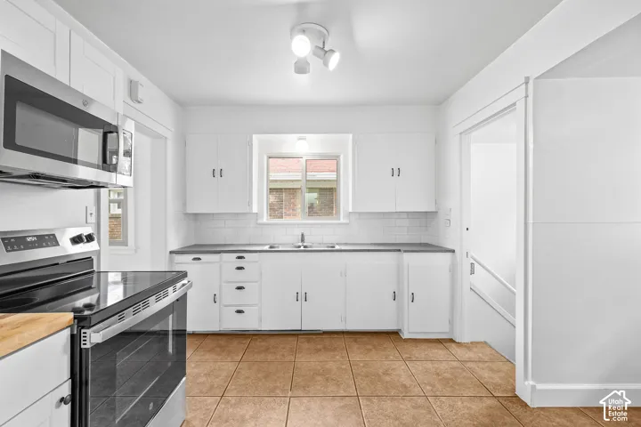 White shaker cabinetry, stainless steel appliances, tiled backsplash, dark countertops, and tiled flooring