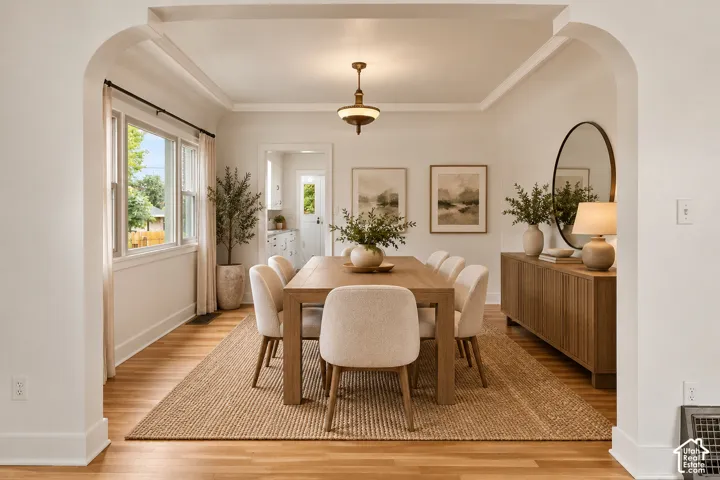 Dining area featuring arched entryways, wood-finish flooring, crown molding, and a central pendant light fixture