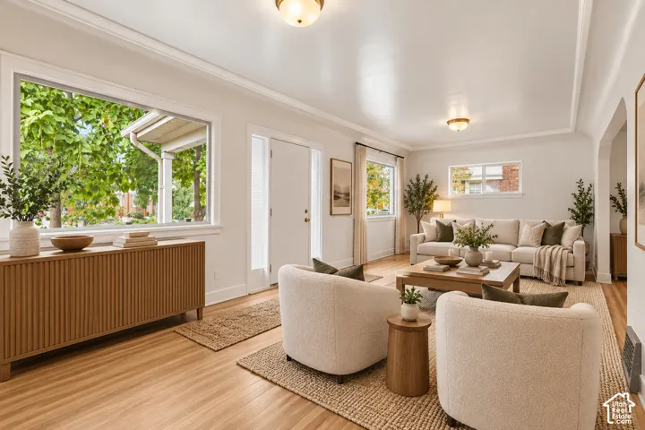 Living area featuring wood-finish flooring, crisp crown molding, large picture windows, and dual ceiling-mounted light fixtures