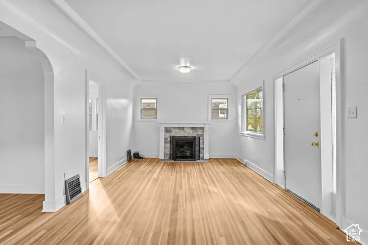 Hardwood flooring, decorative fireplace with stone surround, arched doorway, crown molding, and recessed ceiling light fixture