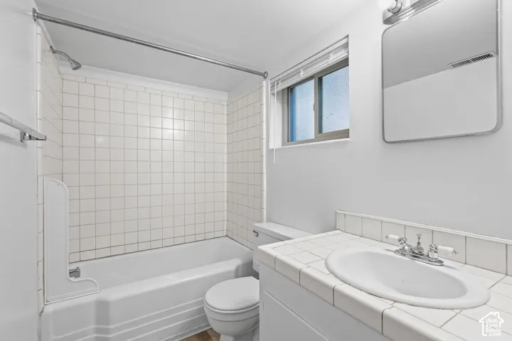 White square tile backsplash and vanity top, inset sink, chrome-finish faucet, rectangular mirror, and a window with blinds