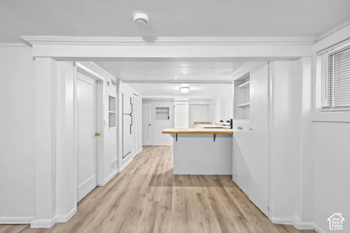 Wood-finish flooring throughout, featuring crown molding, built-in cabinetry, and a window with blinds