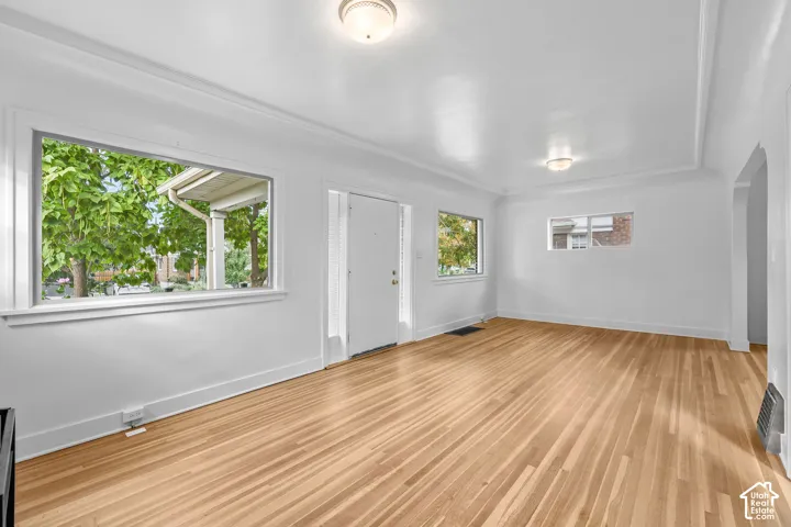 Hardwood flooring, crisp white walls, crown molding, multiple windows, and flush mount lighting