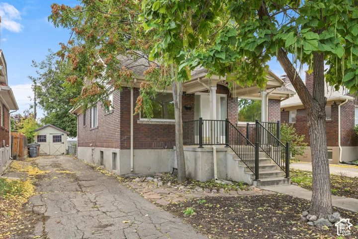 Brick exterior with white trim, covered front porch, concrete steps with black railings, and an accessory shed