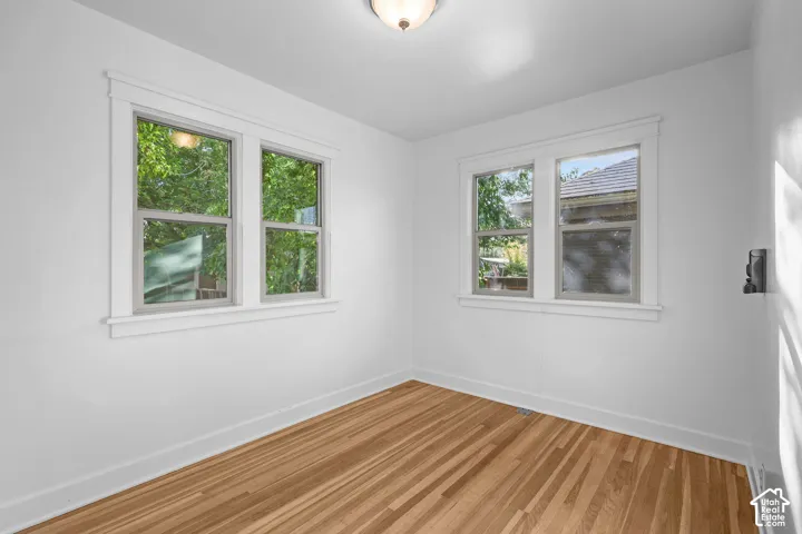 White walls, wood-finish flooring, two window units with white trim, and a flush mount ceiling light