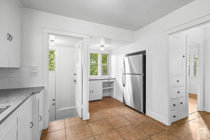 Tiled flooring, white subway tile backsplash, white cabinetry, stainless steel refrigerator, and built-in storage with drawers