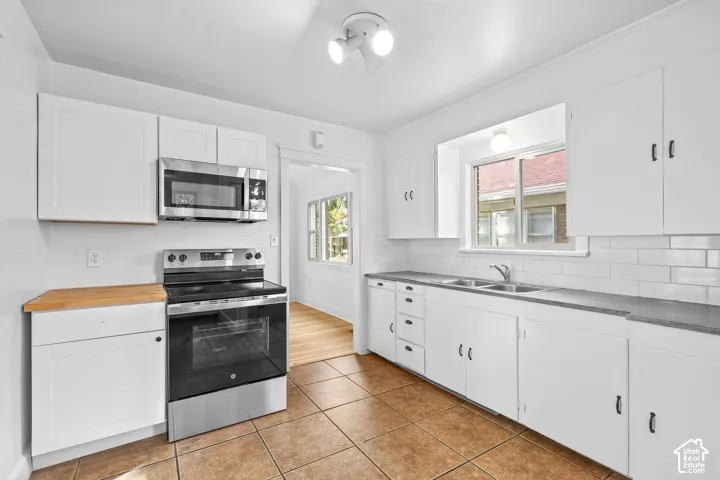 Kitchen featuring white cabinetry, stainless steel appliances, solid surface countertops, a white subway tile backsplash, and tile flooring