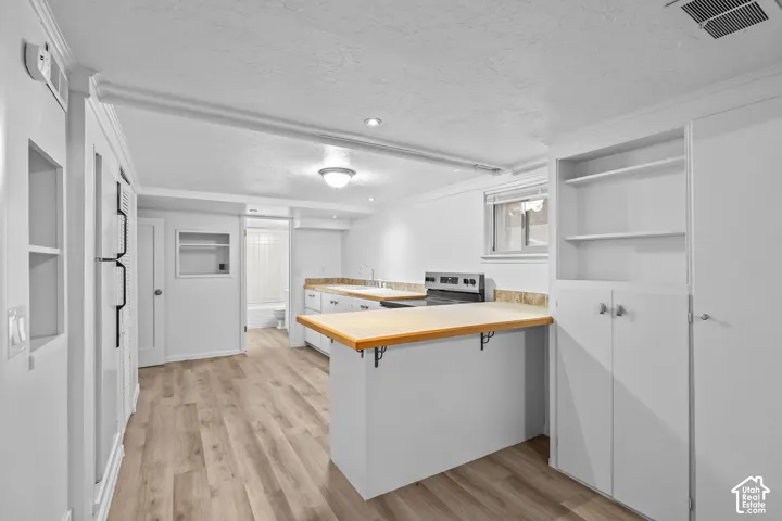 Wood-finish flooring, built-in shelving, white cabinetry, and stainless steel range