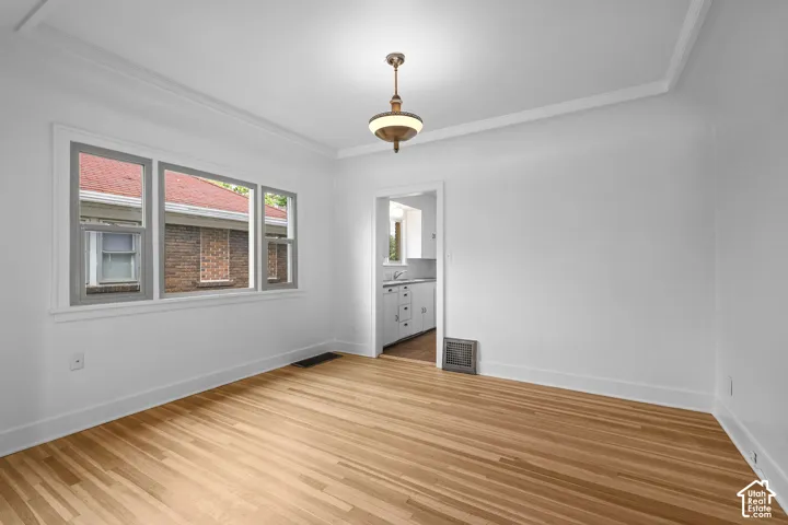 Hardwood flooring, crown molding, white walls, three windows with gray trim, and a ceiling-mounted light fixture