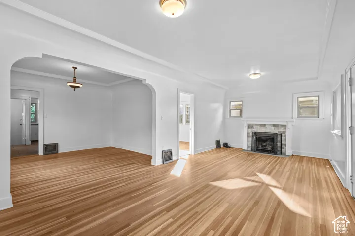 Hardwood flooring throughout, arched doorway, recessed ceiling detail, stone-surround fireplace, and two windows