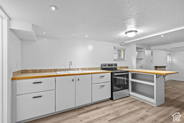 White cabinetry with integrated stainless steel appliances, wood-finish flooring, and recessed lighting