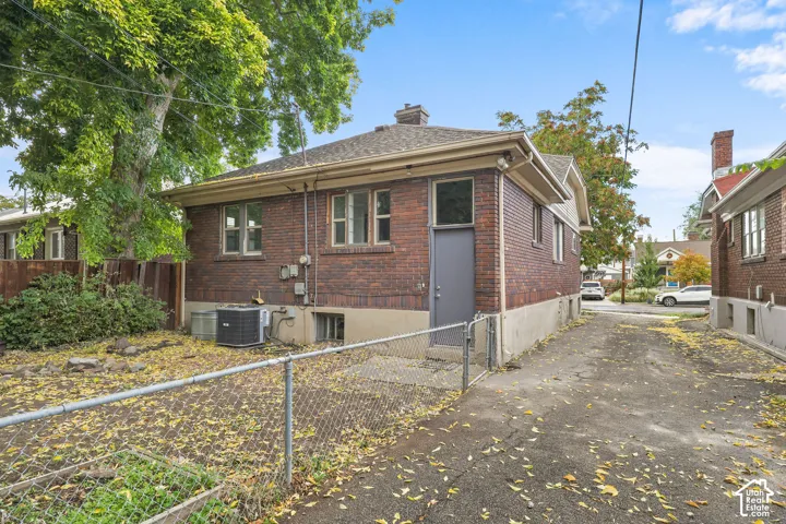 Brick exterior with a gabled roof and a side entrance, featuring a chain-link fence and paved driveway