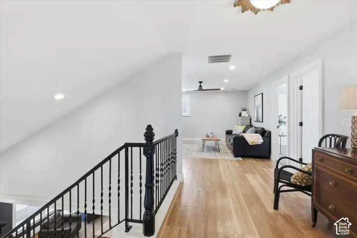Hardwood flooring throughout, recessed lighting, ceiling fan, black wrought iron stair railing, and a white interior door