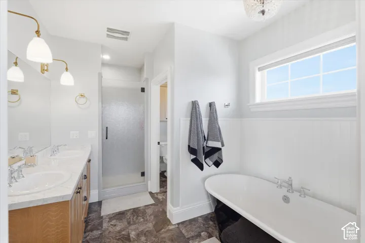 Dual vanity with undermount sinks and light-toned countertops, freestanding bathtub, walk-in shower with clear glass enclosure, and white paneling