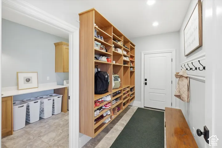 Dedicated mudroom and laundry area featuring custom wood-finish cabinetry with open shelving, built-in cubbies for organized storage, a utility sink with wood-finish vanity, and a green entry mat