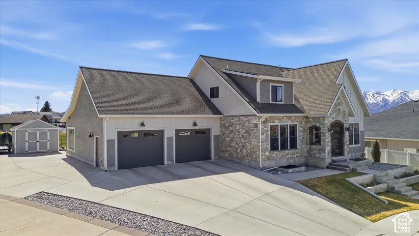 Stone and siding exterior with a multi-level roofline, featuring an attached two-car garage, a separate storage shed, and a concrete driveway