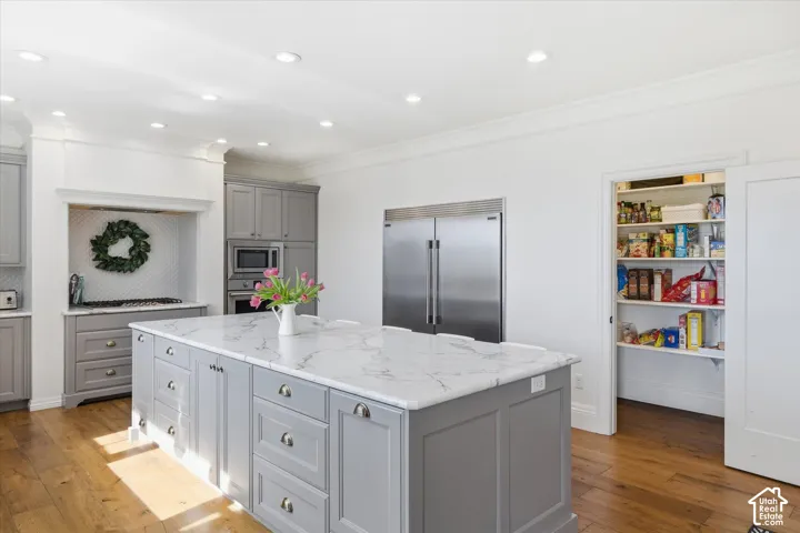Chef's kitchen featuring a large center island with white quartz countertops, gray cabinetry with brushed nickel hardware, stainless steel side-by-side refrigerator, large pantry with door, recessed ceiling lighting, and hardwood flooring throughout the o