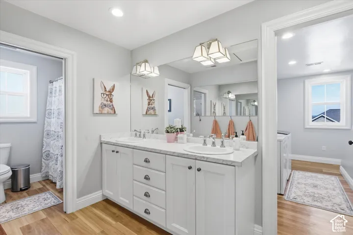 Dual vanity with white cabinetry and chrome fixtures, granite-finish countertop, and wood-finish flooring