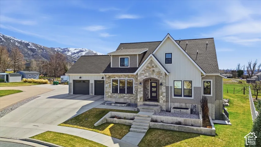Stone and siding exterior with a multi-gabled roof, featuring a two-car garage, a concrete driveway, and tiered landscaping
