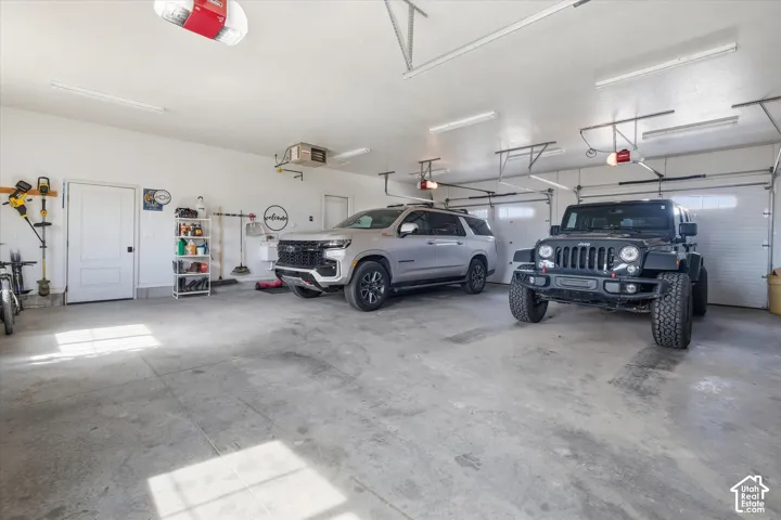 Spacious three-car garage featuring a concrete floor, bright overhead lighting, and two overhead garage doors with openers
