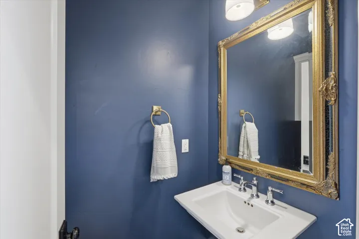 Pedestal sink with chrome faucet, ornate gold-framed mirror, and brass towel ring