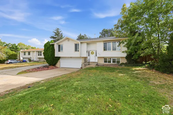 Split-level residence featuring a white facade, an attached garage, a front entry with a small porch, and a sloped front yard