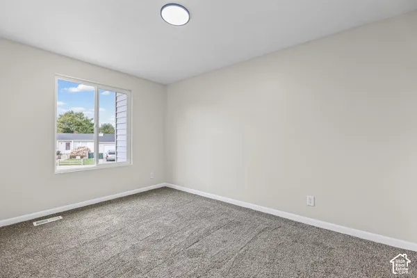 Bright, neutral bedroom featuring neutral carpet flooring, a large window with natural light, and recessed ceiling lighting