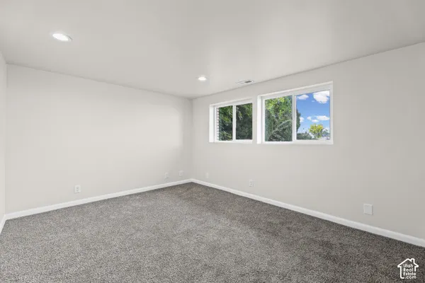 Recessed lighting, light gray wall paint, gray carpeting, and two white-framed windows