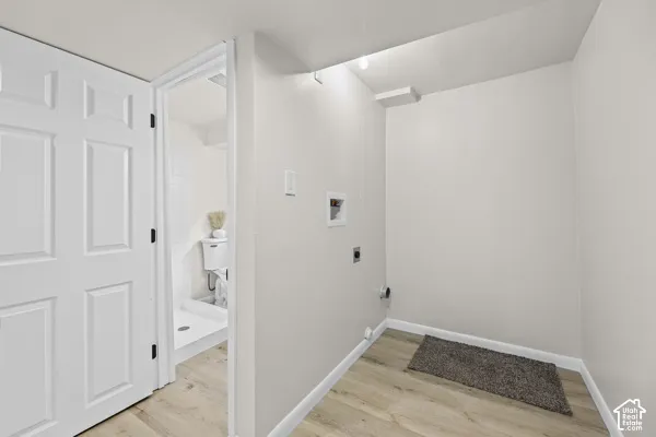Utility area with light wood-finish flooring, white paneled door, and neutral wall tones