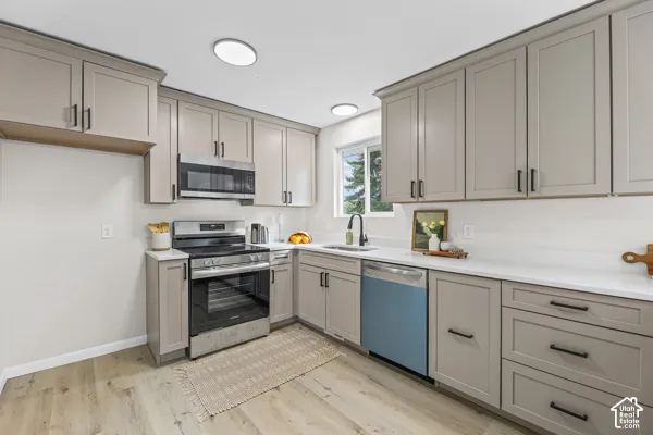 Kitchen featuring shaker-style cabinetry, stainless steel appliances, a window above the sink, light-toned countertops, and wood-finish flooring