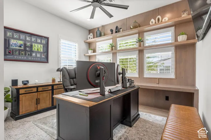 Built-in wood-finish shelving, multiple windows with plantation shutters, wood-finish flooring, and a ceiling fan with integrated lighting