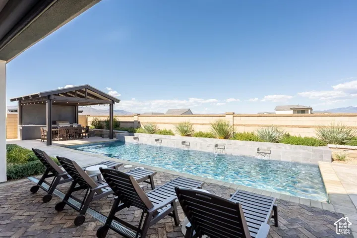 In-ground swimming pool with multiple water features, paver patio, covered outdoor dining area, and built-in outdoor kitchen