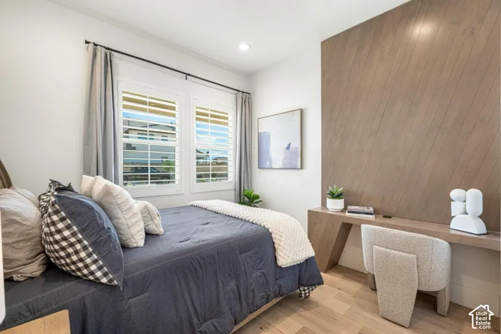 Hardwood-style flooring, dual windows with plantation shutters, recessed lighting, and a built-in wood-finish desk with an accent wall
