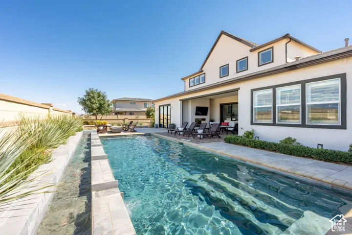 Swimming pool with integrated steps, adjacent hardscaping, and a covered patio area with an outdoor fireplace