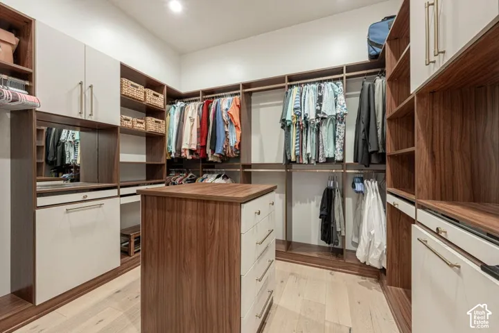 Custom closet system featuring wood-finish cabinetry, integrated shelving, hanging rods, an island with drawers, and wood-finish flooring