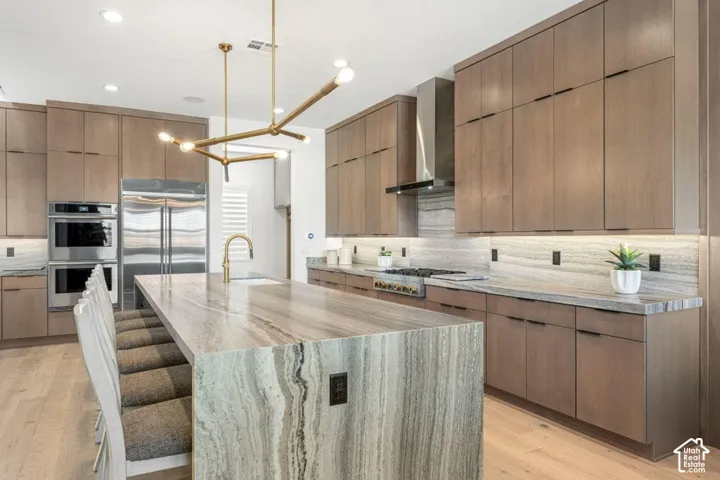 Gourmet kitchen with a waterfall island, integrated stainless steel appliances, contemporary wood cabinetry, under-cabinet lighting, and a linear brass chandelier