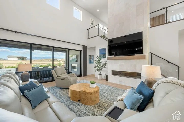 Vaulted ceilings with clerestory windows, a full-height stone-clad fireplace, sliding glass door access to the exterior, wood-finish flooring, and a glass-paneled staircase