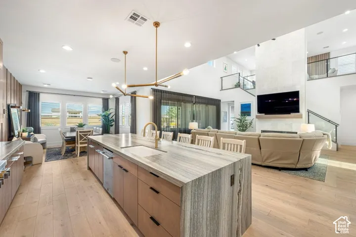 Open-concept living space with light wood-finish flooring, a kitchen island with an integrated sink, and an exposed fireplace