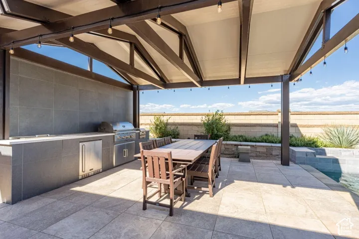 Expansive outdoor living area featuring a covered patio, built-in BBQ, stainless steel outdoor refrigerator, and a pool