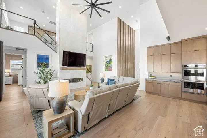 Vaulted ceiling great room with wood-finish flooring, a two-story fireplace, and built-in cabinetry featuring integrated double ovens and stone countertops