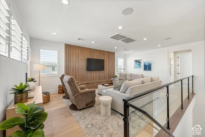 Recessed lighting, wood-finish flooring, custom wood-slat accent wall, and a glass panel railing with a dark-finish top rail