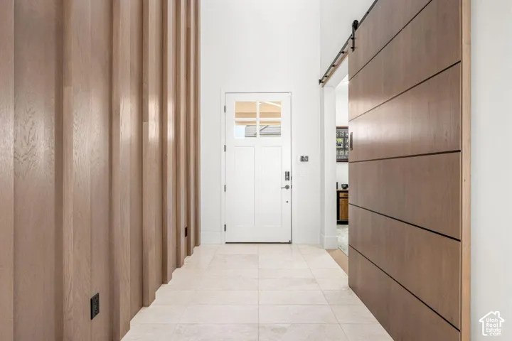 Entryway featuring a white paneled door with transom window, tile flooring, a slatted wood-finish accent wall, and a large wood-finish barn door